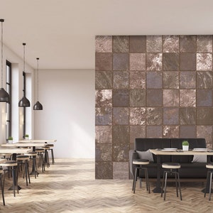 Puede incluir: Un interior de cafetería moderno con un sofá de cuero negro y una pared cubierta de azulejos cuadrados marrones y grises. La cafetería tiene un suelo de madera y sillas de metal negro alrededor de las mesas.