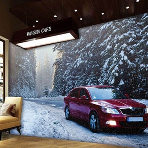 May include: A red car drives on a snowy road through a forest of snow-covered pine trees. The car has a black interior and a black license plate. The sign above the road reads "Wansha Cafe".