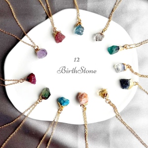 May include: Twelve gold necklaces with different coloured gemstone pendants. The necklaces are arranged in a circle on a white plate. The text "12 Birthstone" is written in the centre of the plate.