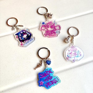May include: Four acrylic keychains with silver key rings. Each keychain features a different design with colorful graphics and text. One keychain says "I'M NOT WEAK!" and another says "JINX WAS HERE!"