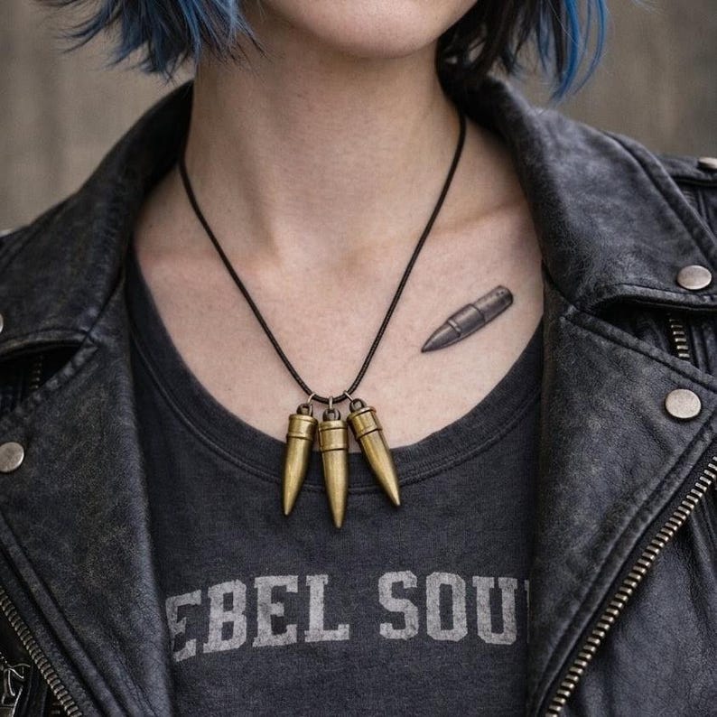 Pu&ograve; includere: Una collana con cordino nero con tre ciondoli a forma di proiettile color oro. La persona indossa una maglietta grigia con la scritta "REBEL SOUL" e una giacca di pelle nera. Un tatuaggio a forma di proiettile &egrave; visibile sul petto.