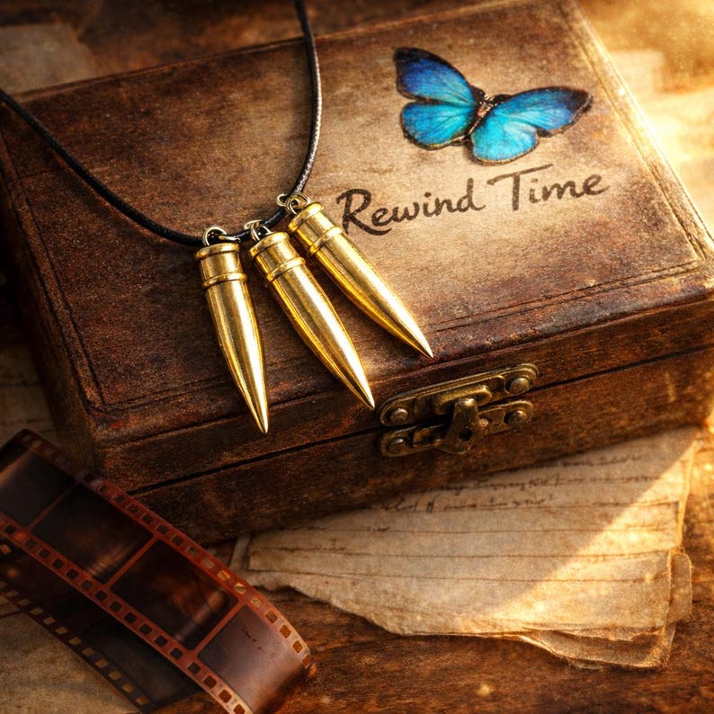 Pu&ograve; includere: Una collana con pendente a proiettile dorato con tre ciondoli a proiettile. La collana &egrave; appesa sopra una scatola di legno vintage con le parole "Rewind Time" e una farfalla blu. Una striscia di pellicola si trova nelle vicinanze.