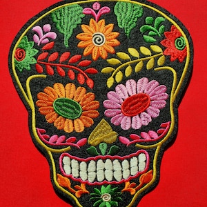 May include: Black embroidered sugar skull patch with colorful flowers and leaves. The skull has a white smile and green eyes.
