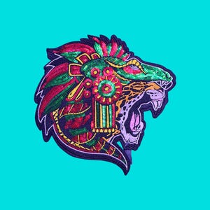 May include: A decorative patch featuring a stylized jaguar head in profile, adorned with vibrant sequins in shades of emerald green, magenta, and gold. The design includes intricate geometric patterns and a roaring mouth with visible teeth.
