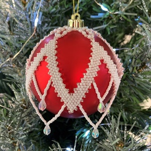 May include: A red Christmas ornament with a white beaded design and crystal drops hanging from the bottom.