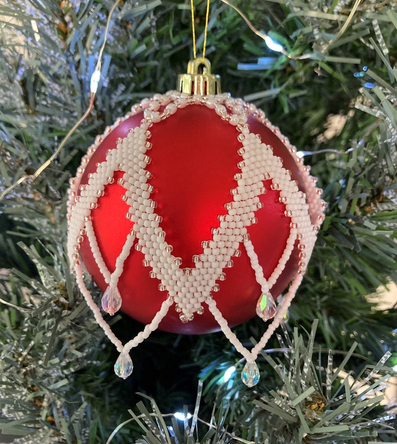 May include: A red Christmas ornament with a white beaded design and crystal drops hanging from the bottom.