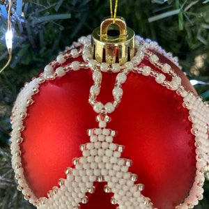 May include: A red Christmas ornament with a white beaded design. The ornament is decorated with a white beaded snowflake pattern.
