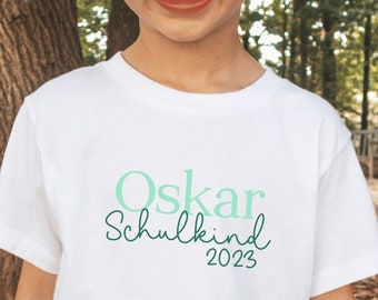 weißes T-Shirt „Schulkind 2023“ personalisiert mit Name, gedruckt in Wunschfarbe I Geschenk zur Einschulung I 100% Baumwolle