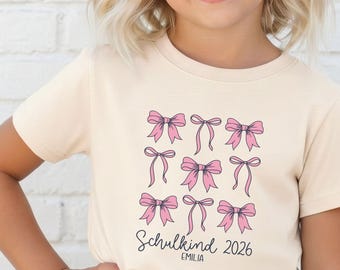 Schleifen Schulkind 2026 Statement T-Shirt, personalisiert mit Name, Druckposition & Druckfarbe I Einschulungsgeschenk