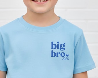 May include: A light blue t-shirt with the words "big bro." and the year "2026" printed in blue. The shirt is short-sleeved and has a crew neck.