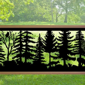 May include: A black metal outdoor fence panel featuring a forest silhouette design. The panel depicts trees, an owl, and wildlife, set within a wooden frame. The background shows a green lawn and trees.