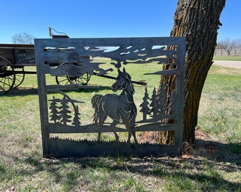 May include: A metal silhouette of a horse standing in a field with trees. The silhouette is cut out of a metal sheet and is mounted on a wooden post. The horse is facing to the right and has a long mane and tail. The trees are in the background and are silhouetted against a cloudy sky.