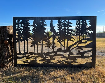 May include: A black metal silhouette of a forest scene with trees and a stream. The silhouette is cut out of a metal sheet and is mounted on a wooden post.