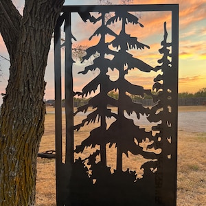 May include: A black metal silhouette of three pine trees cut out against a sunset sky. The silhouette is mounted on a black metal frame.