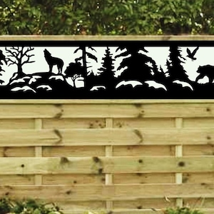 May include: A black metal fence panel with a cutout design of a forest scene. The scene includes trees, a wolf howling, a bear walking, and a bird flying. The fence panel is mounted on a wooden fence.