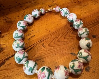 May include: A white porcelain necklace with green and pink floral designs on each bead.