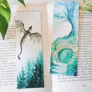 Könnte beinhalten: Zwei Aquarell-Lesezeichen. Eines zeigt eine grüne Tür mit einem Steinbogen und einem grünen Baum. Das andere Lesezeichen zeigt einen schwarzen Drachen, der über einen grünen Wald fliegt.