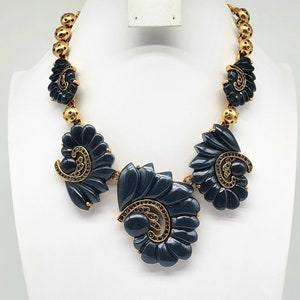 May include: A statement necklace with a gold-tone chain and dark gray, stylized floral pendants. The pendants are accented with gold-tone details and small, black gemstones. The necklace is displayed on a white bust.