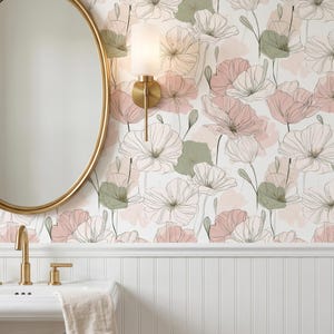 Puede incluir: Interior de baño con lavabo blanco, grifo dorado y espejo ovalado con marco dorado. La pared está adornada con papel pintado floral en rosa, verde y blanco. Una lámpara de pared dorada con pantalla de vidrio esmerilado está montada en la pared.