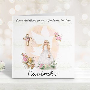 May include: A white card with a pink and white watercolour background featuring a girl in a white dress holding a book. The girl is standing in front of a white dove with a cross behind her. The card says "Congratulations on your Confirmation Day" and "Caoimhe" at the bottom.