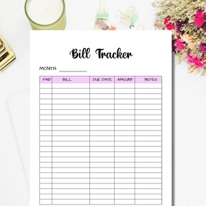 May include: A white paper titled "Bill Tracker" with a pink header and columns for tracking bills. The columns are labeled "Paid", "Bill", "Due Date", "Amount", and "Notes". The paper is surrounded by office supplies and flowers.