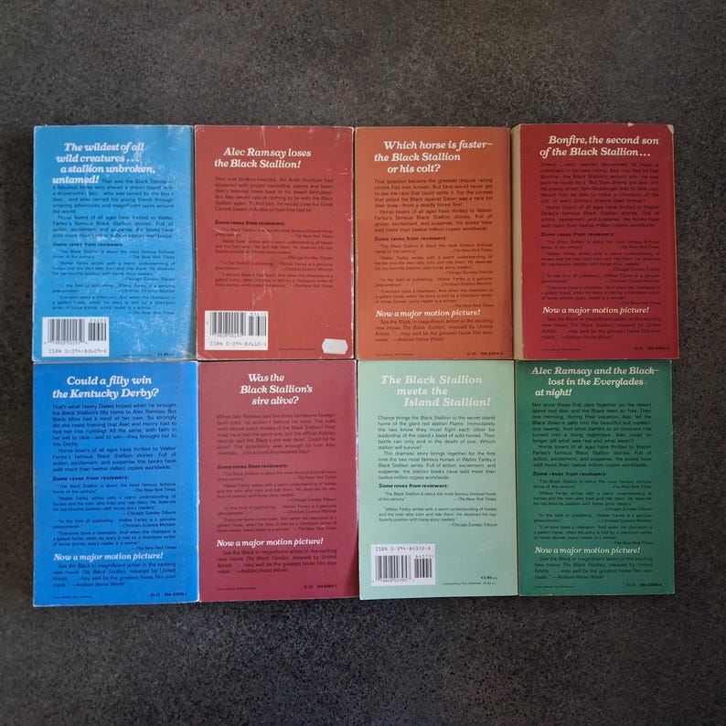 May include: A collection of vintage paperback books with colorful covers. Titles include "The Black Stallion" series, featuring text and illustrations. The books are arranged on a neutral surface, showcasing their spines and back covers.