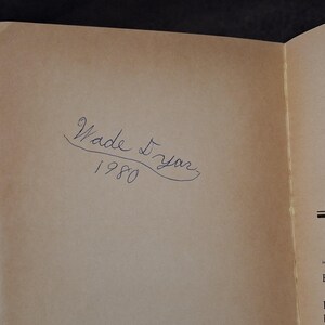 May include: An open book page with the handwritten inscription "Wade Dyar 1980" in blue ink. The paper has a light brown color.