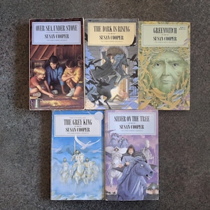 May include: A collection of five paperback books from The Dark Is Rising sequence by Susan Cooper, including Over Sea, Under Stone, The Dark Is Rising, Greenwitch, The Grey King, and Silver on the Tree, each featuring distinct cover illustrations.
