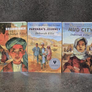 Peut inclure: Trois livres de Deborah Ellis sont présentés. Les titres sont "The Breadwinner", "Parvana's Journey" et "Mud City". Les couvertures présentent des illustrations d'enfants et de paysages désertiques. "Parvana's Journey" a reçu le prix Jane Addams Children's Book Award.