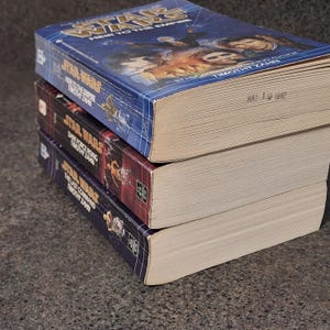 Op de afbeelding: Drie Star Wars-romans op elkaar gestapeld. Het bovenste boek heet "Heir to the Empire" van Timothy Zahn, met een blauwe omslag. Het middelste boek is "Dark Force Rising" en het onderste boek is "The Last Command".