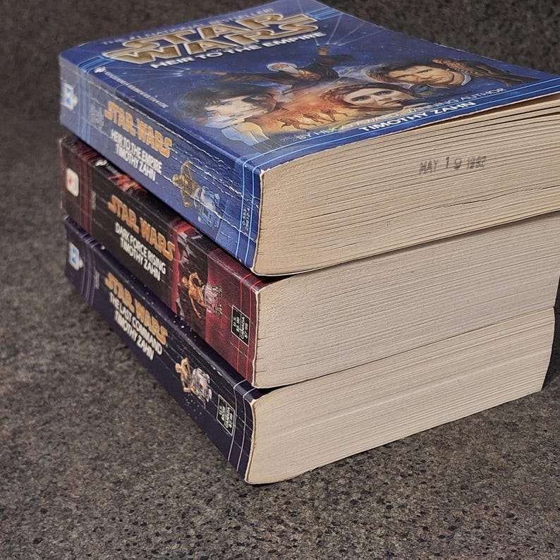 Op de afbeelding: Drie Star Wars-romans op elkaar gestapeld. Het bovenste boek heet "Heir to the Empire" van Timothy Zahn, met een blauwe omslag. Het middelste boek is "Dark Force Rising" en het onderste boek is "The Last Command".