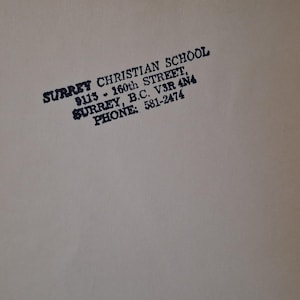 May include: A close-up of a beige surface with black text. The text reads "SURREY CHRISTIAN SCHOOL, 9113 - 160th STREET, SURREY, B.C. V3R 4N4 PHONE: 581-2474."
