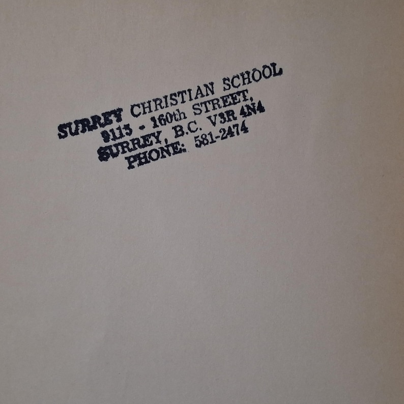 May include: A close-up of a beige surface with black text. The text reads "SURREY CHRISTIAN SCHOOL, 9113 - 160th STREET, SURREY, B.C. V3R 4N4 PHONE: 581-2474."