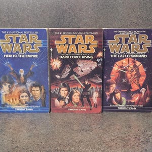 Op de afbeelding: Drie Star Wars-romans: "Erfgenaam van het Keizerrijk", "Duistere Kracht Rijst" en "Het Laatste Commando". Elk boek heeft een omslag met karakterportretten en ruimtesc&egrave;nes. De titels zijn vetgedrukt, met de naam van de auteur onderaan.