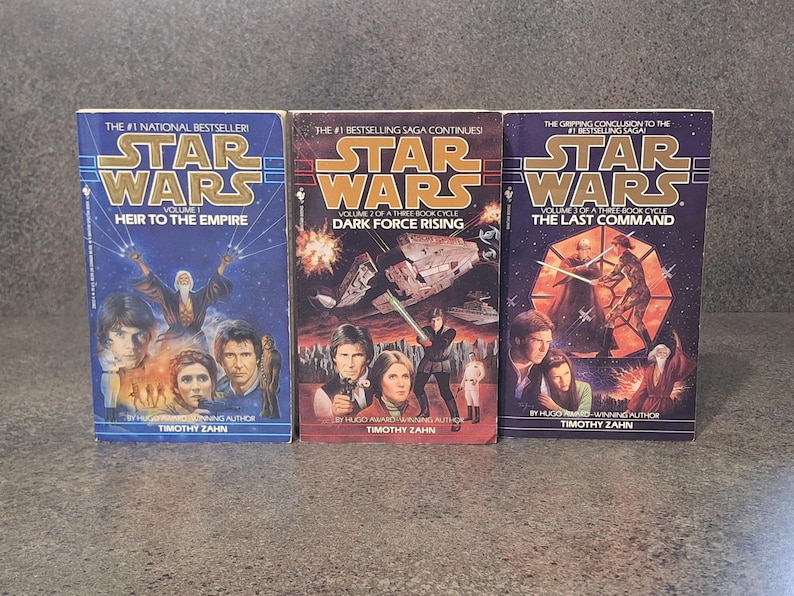 Op de afbeelding: Drie Star Wars-romans: "Erfgenaam van het Keizerrijk", "Duistere Kracht Rijst" en "Het Laatste Commando". Elk boek heeft een omslag met karakterportretten en ruimtesc&egrave;nes. De titels zijn vetgedrukt, met de naam van de auteur onderaan.