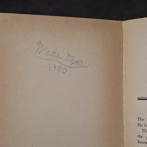 May include: An open book with a light brown page. The handwritten text "Wade Syar 1980" is in black ink. The page is slightly aged, with a visible crease.