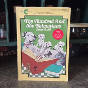 Peut inclure: Un livre de poche vintage intitulé "The Hundred and One Dalmatians" de Dodie Smith. La couverture présente des illustrations de chiens dalmatiens, de chiots et d'un chat. Le livre est jaune avec des accents verts et rouges, avec le texte "Over Two Million Copies in Print!"