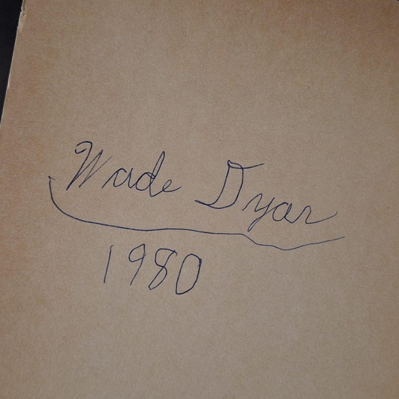 May include: A handwritten inscription in blue ink on a tan paper background. The inscription reads "Wade Dyar" above the year "1980". The handwriting is cursive and the numbers are simple.