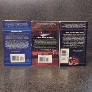 Op de afbeelding: Drie Star Wars-romans worden getoond, met titels als "Beware the Dark Side" en "Dark Force Rising". De boeken hebben kleurrijke covers met tekst en afbeeldingen, tegen een donkere achtergrond. De ruggen zijn zichtbaar en tonen de branding van de serie.