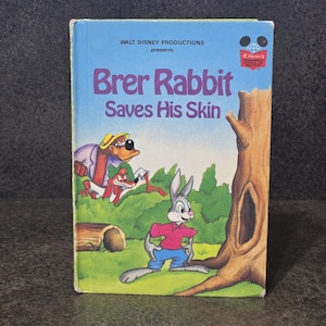 May include: A vintage hardcover book titled "Brer Rabbit Saves His Skin" by Walt Disney Productions. The cover features illustrations of Brer Rabbit, a fox, and a bear-like character in a forest setting. The book has a blue background with the title in purple.