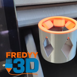 Puede incluir: Un portavasos gris impreso en 3D con un borde naranja. El portavasos tiene un diseño en forma de diamante y está diseñado para caber en un coche.