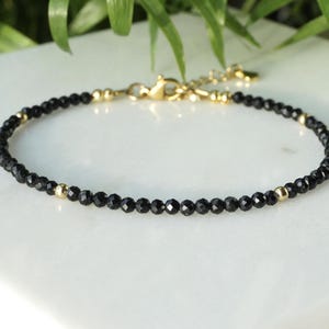 Op de afbeelding: Delicate armband met kleine zwarte kralen en gouden accenten. De armband heeft een goudkleurige sluiting en bestaat uit kleine, ronde zwarte kralen met gouden kralen ertussen. Een eenvoudig sieraad.