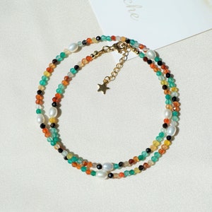 May include: A multi-colored beaded necklace with a gold star charm. The necklace is made with green, orange, yellow, black, and white beads.