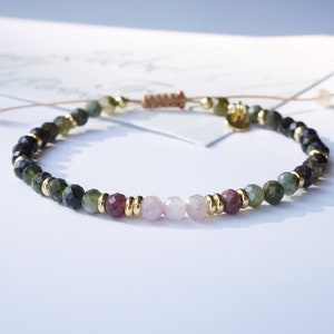 Op de afbeelding: Een armband gemaakt met groene, roze en zwarte edelsteen kralen met gouden accenten.