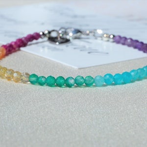 Könnte beinhalten: Ein Regenbogen-Edelstein-Armband mit rosa, orange, gelben, grünen, blauen und violetten Perlen.