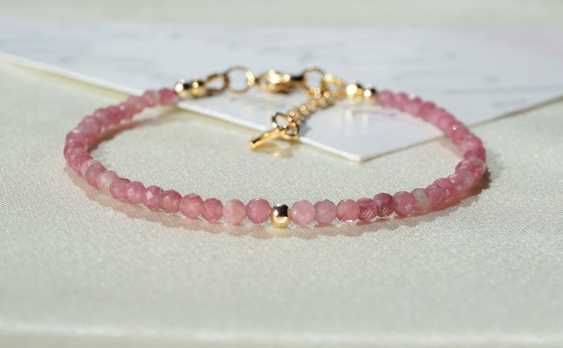 Op de afbeelding: Een delicate armband van roze edelstenen met gouden accenten. De armband is gemaakt van kleine, gefacetteerde kralen en heeft een eenvoudig, elegant ontwerp.