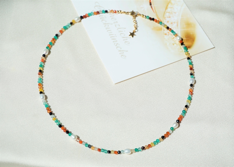 May include: A colorful beaded necklace with a star charm. The necklace features green, orange, black, and white beads.