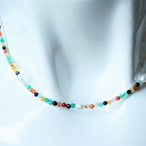 May include: A multi-colored beaded necklace with green, red, orange, black, and white beads. The necklace is on a white mannequin.