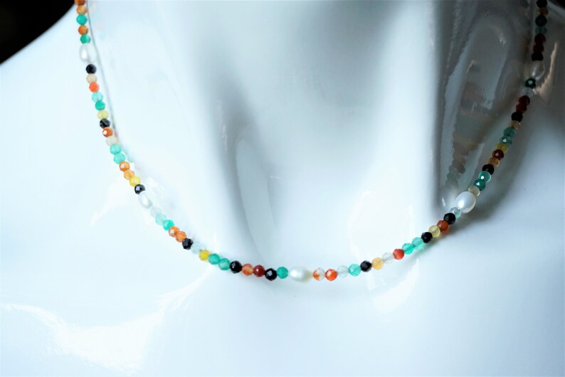 May include: A multi-colored beaded necklace with green, red, orange, black, and white beads. The necklace is on a white mannequin.