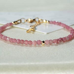 Op de afbeelding: Een delicate armband van roze edelstenen met een gouden sluiting en een enkele gouden kraal. De armband is gemaakt van kleine, ronde kralen en is perfect voor dagelijks gebruik.